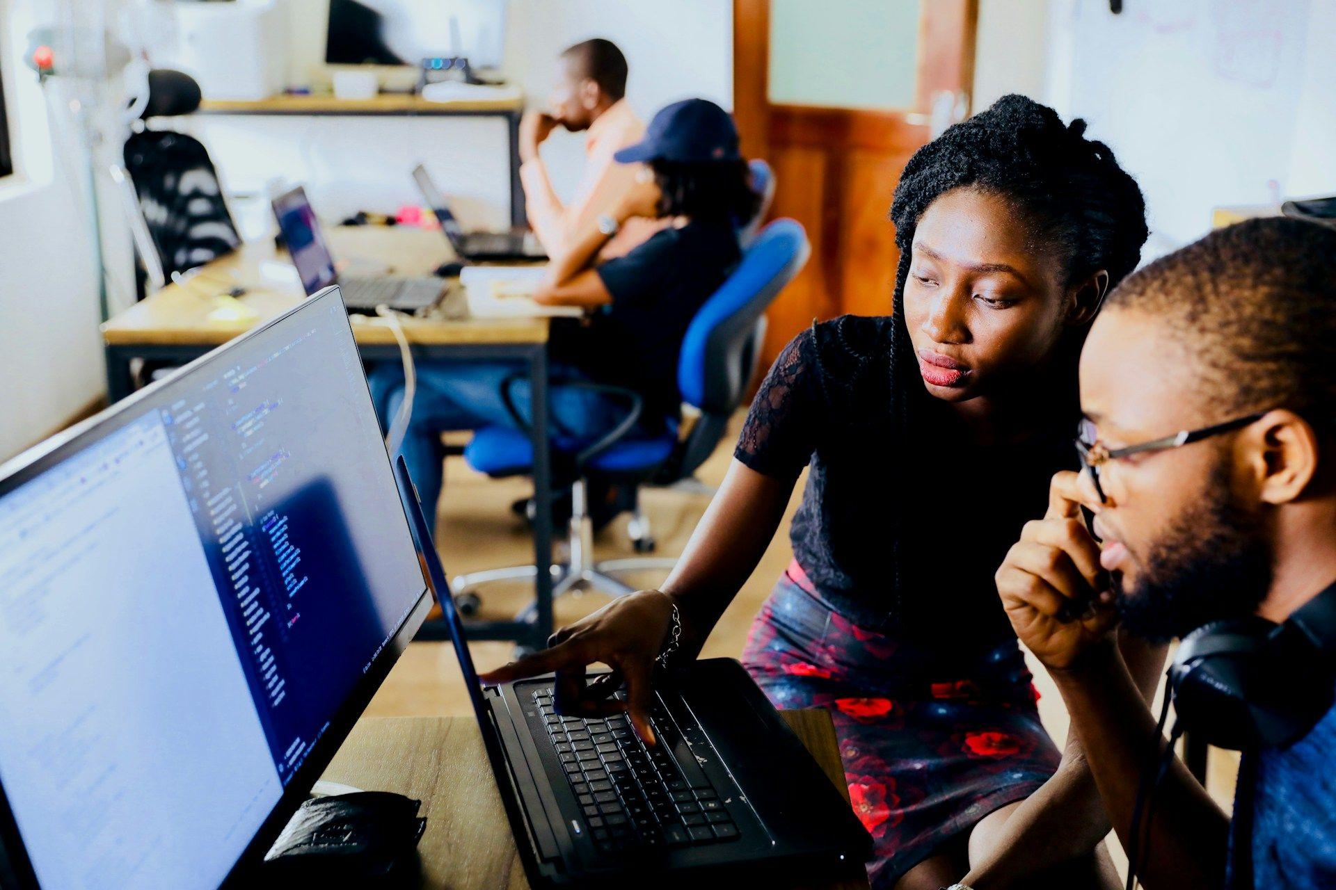 Two people sitting in front of monitor looking at code.